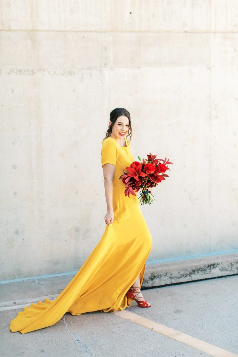 Original, gul brudekjole med tog og ærmer, røde sko og en rød brudebuket