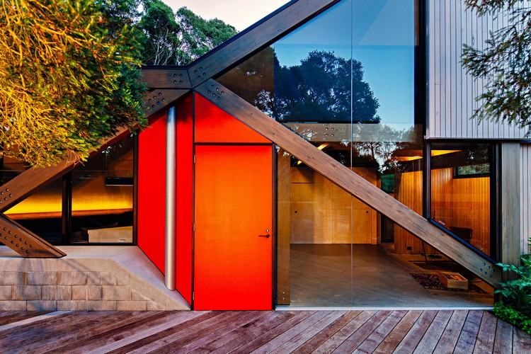 design sommerhus skråtag kystskov moderne bjerghytte usædvanlig form træ veranda indgangsdør glasvindue