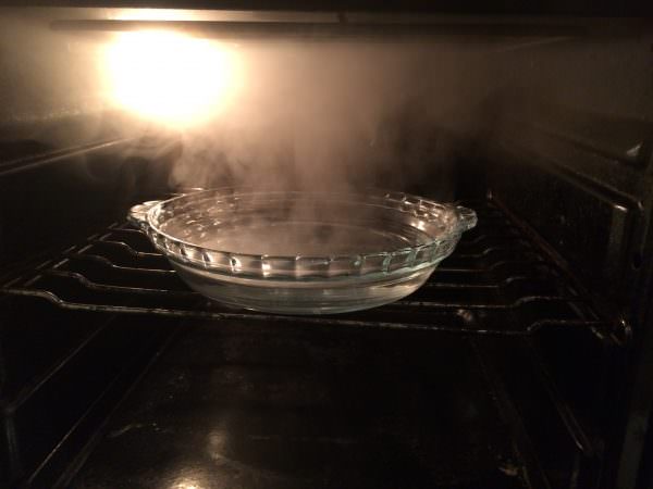 Før du begynner å rengjøre ovnen, må du forvarme den og legge en gryte med varmt vann i den og tilsette litt eddik.