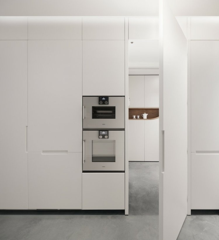 Minimalistisk hvidt køkken med høj ovn og indbyggede skabe
