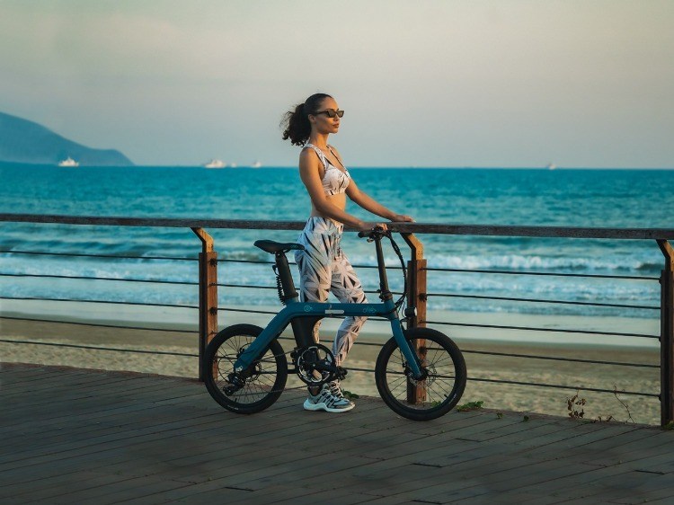 kvinde med sammenklappelig elektrisk cykel nyder solnedgangen på stranden