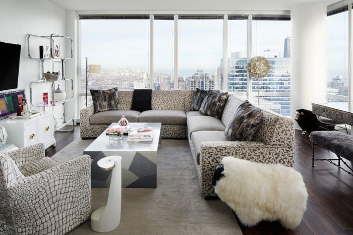 Pohovka s polštáři v šedých a béžových barvách v obývacím pokoji s velkými okny