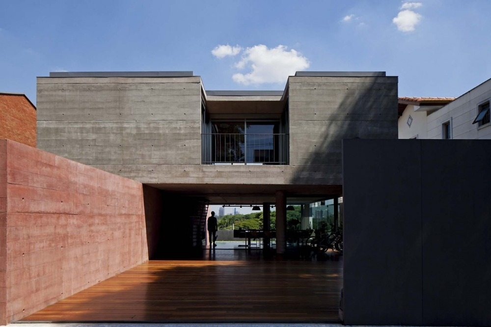 Trægulv i det udvendige område med en væg af rødfarvet beton i et minimalistisk hus