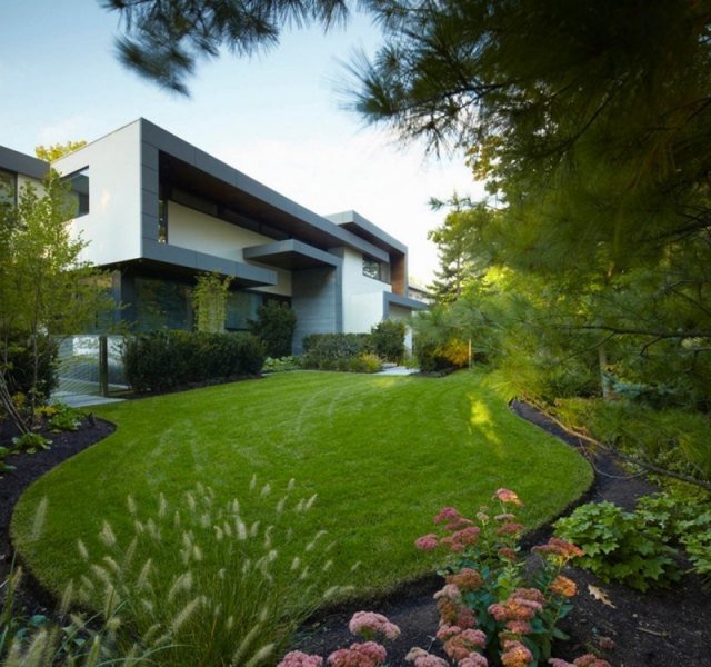 Moderne hus med fladt tag med græsplæne i haven, der lægger blomsterbed