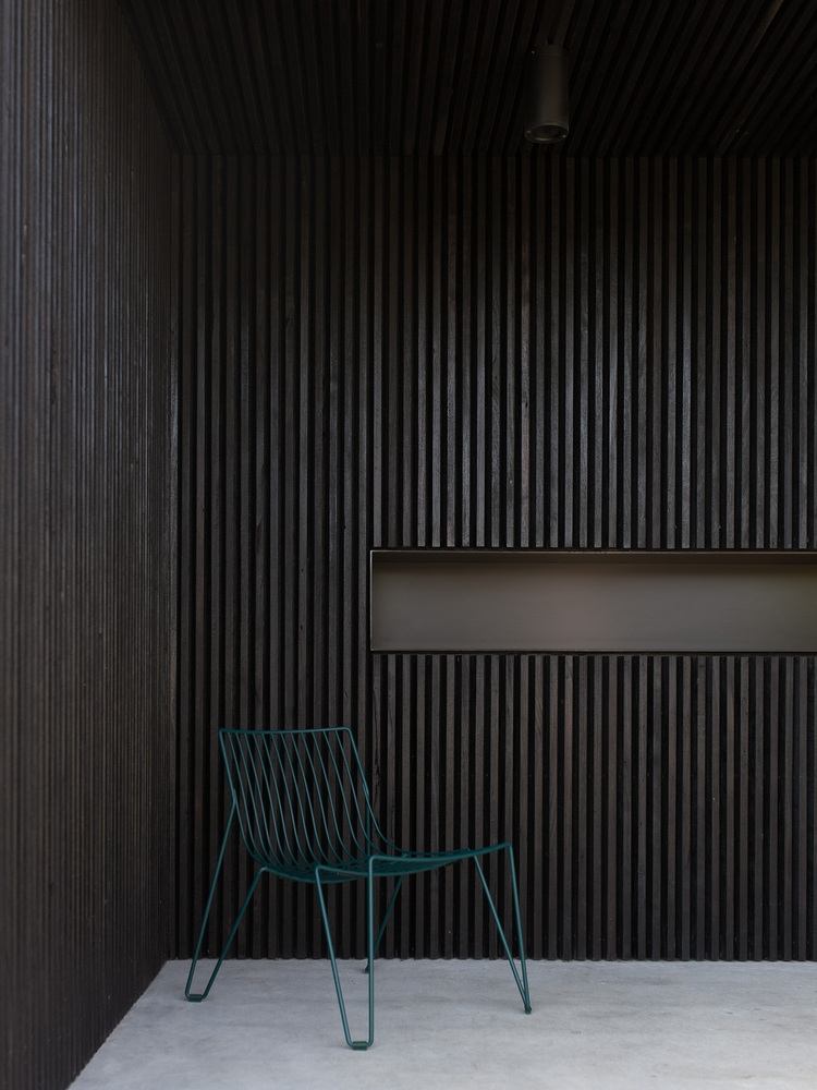 udendørs terrasse med mørke trælameller som facadebeklædning med designerstol i blåt