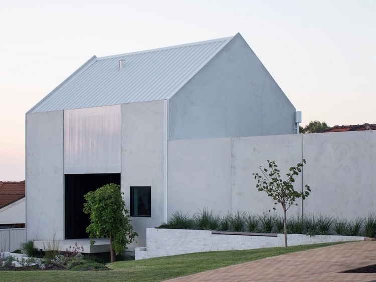 minimalistisk designerhave med græsplæne og træer foran huset med betonvægge og et skråt tag