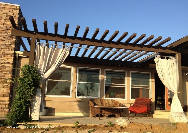 træ-pergola-gardiner-natursten-væg-træ-konstruktion-mørk-sofa-lænestol-jern-rattan