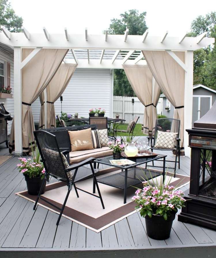 træ-pergola-gardiner-hvid-sort-planke-gulv-havemøbler-metal-puder-beige-planter-tæppe