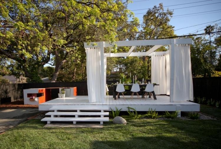 Træpergola -gardiner-hvide-spisebord-stole-have-græsplæne-træer-smukke