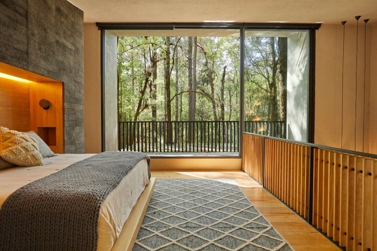 komfortabelt udseende soveværelse med et stort vindue med udsigt over skoven