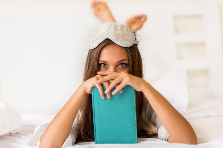 ung kvinde i sengen med sovemaske og bog