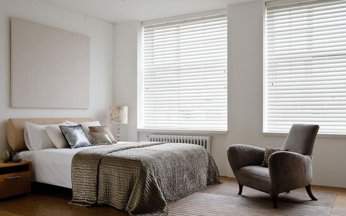 Vita horisontella persienner i sovrummet med ett grått överkast