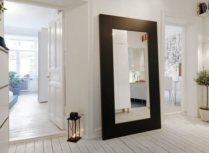Speil i en bred svart ramme på gulvet i en hvit korridor