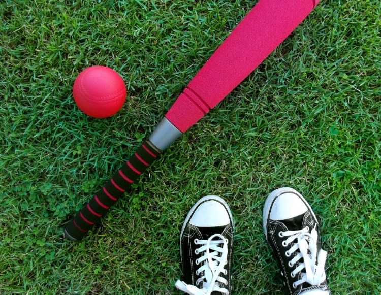 pink baseballbat og bold ved siden af ​​sneakers på grønt græs
