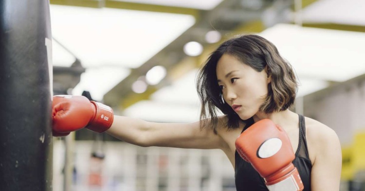 Asiatisk kvinde, der slår boksesæk med boksehandsker i et sportsrum