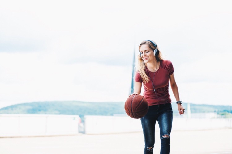 smilende ung kvinde med hovedtelefoner og basketball som en sport for at tabe sig