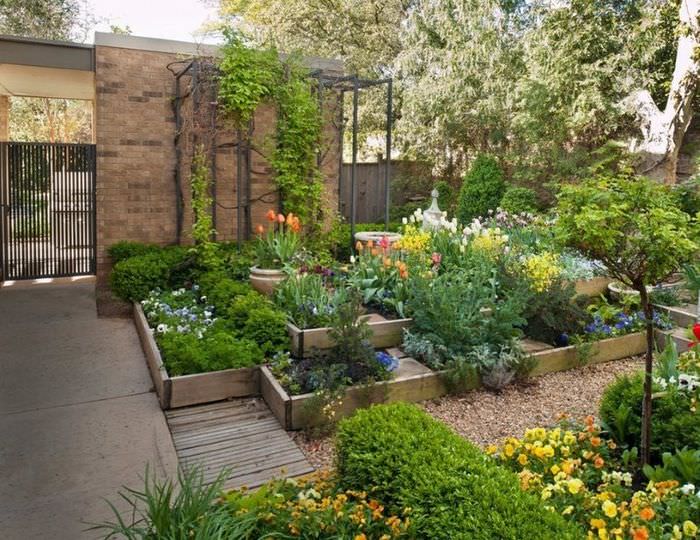 Høye blomsterbed laget av høvlede brett på gårdsplassen til sommerhuset