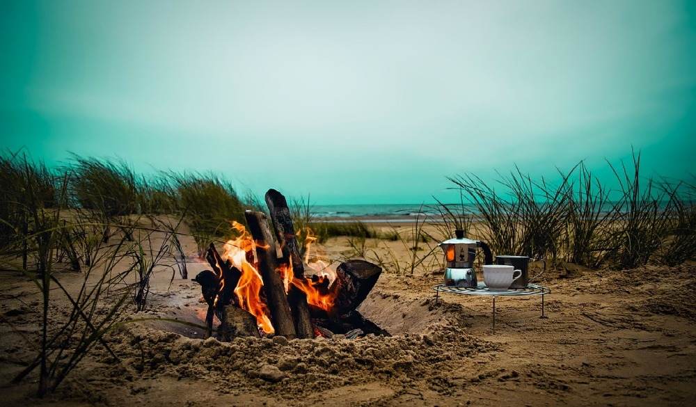 brændende bålopskrifter på stranden med kaffe og madlavning grillcamping