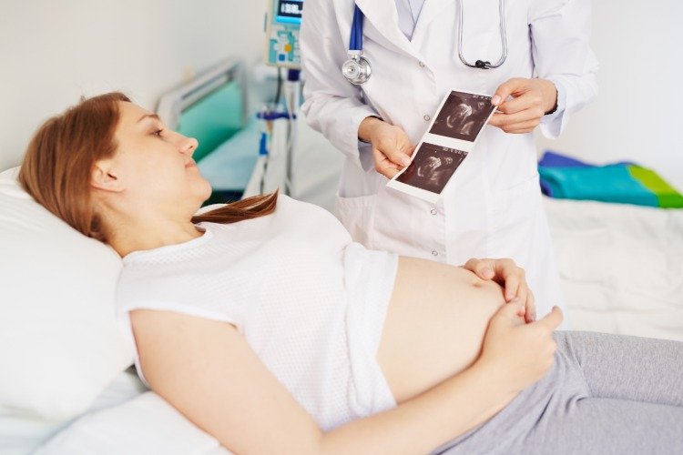 læge viser billede af foster på hospitalet til gravid kvinde i sengen
