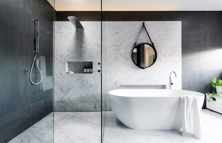 Moderne badeværelser i gråt med granitvægfliser og fritstående badekar og rundt spejl og brusekabine med glasskillevæg