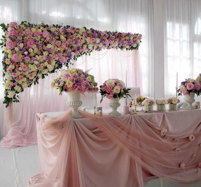 Zdobenie svadobného stolu svetlými kvetmi a priesvitnou látkou