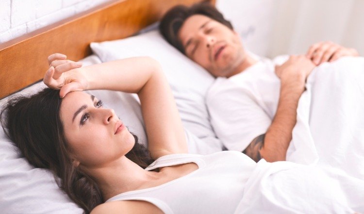 ung kvinde ligger søvnløs i sengen ved siden af ​​en mand