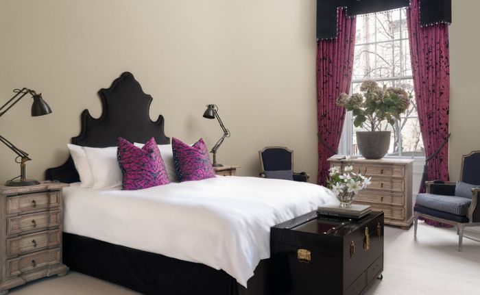 Weiße Tagesdecke auf einem schwarzen Bett und Kissen in lila Bezügen